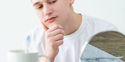Perfect skin. Facial treatment. Morning shave. Cheerful attractive young man touching flawless clean face admiring mirror reflection on white background.